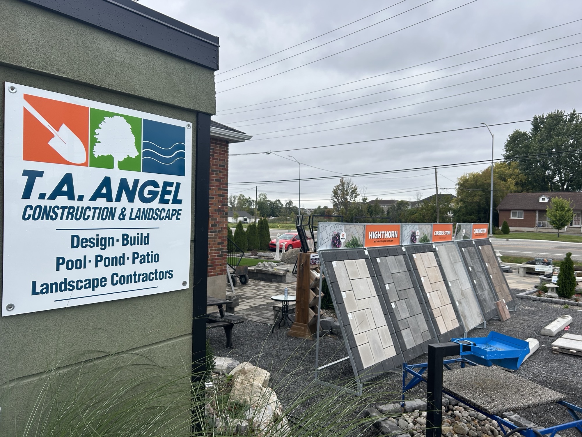 A sign with the text: T.A. Angel Construction and Landscape Design, Build, Pool, Pond, Patio, Landscape Contractors with images of Triple H Concrete products in the background Highthorn, Carrera and Covington